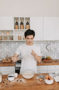 Young man preparing batter in a stylish kitchen setting, surrounded by baking ingredients.