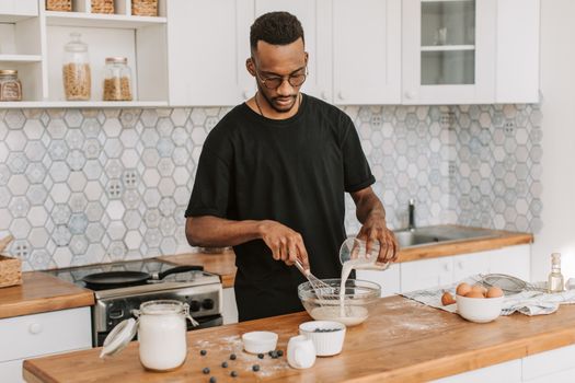 African American man pouring milk into a bowl, preparing food in a contemporary kitchen setting.
