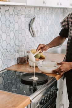 Close-up of a person pouring pancake batter on a stove in a stylish kitchen.