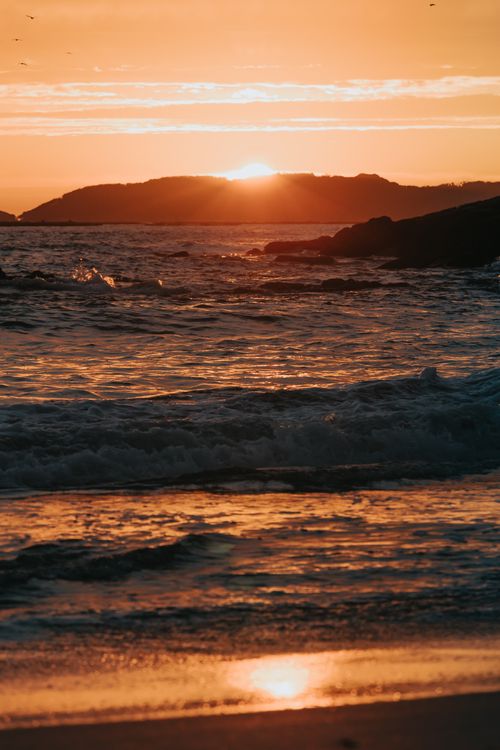 Free A breathtaking sunset over the ocean with waves gently crashing on the shore, capturing the golden glow. Stock Photo