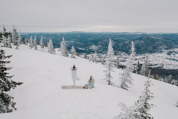 A Couple Meditating In The Snow Covered Mountain