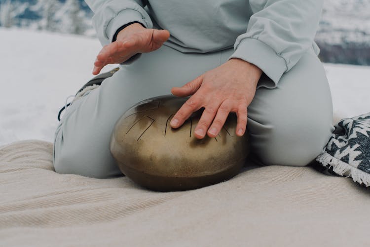 A Person In Gray Sweater And Pants Tapping A Steel Tongue Drum