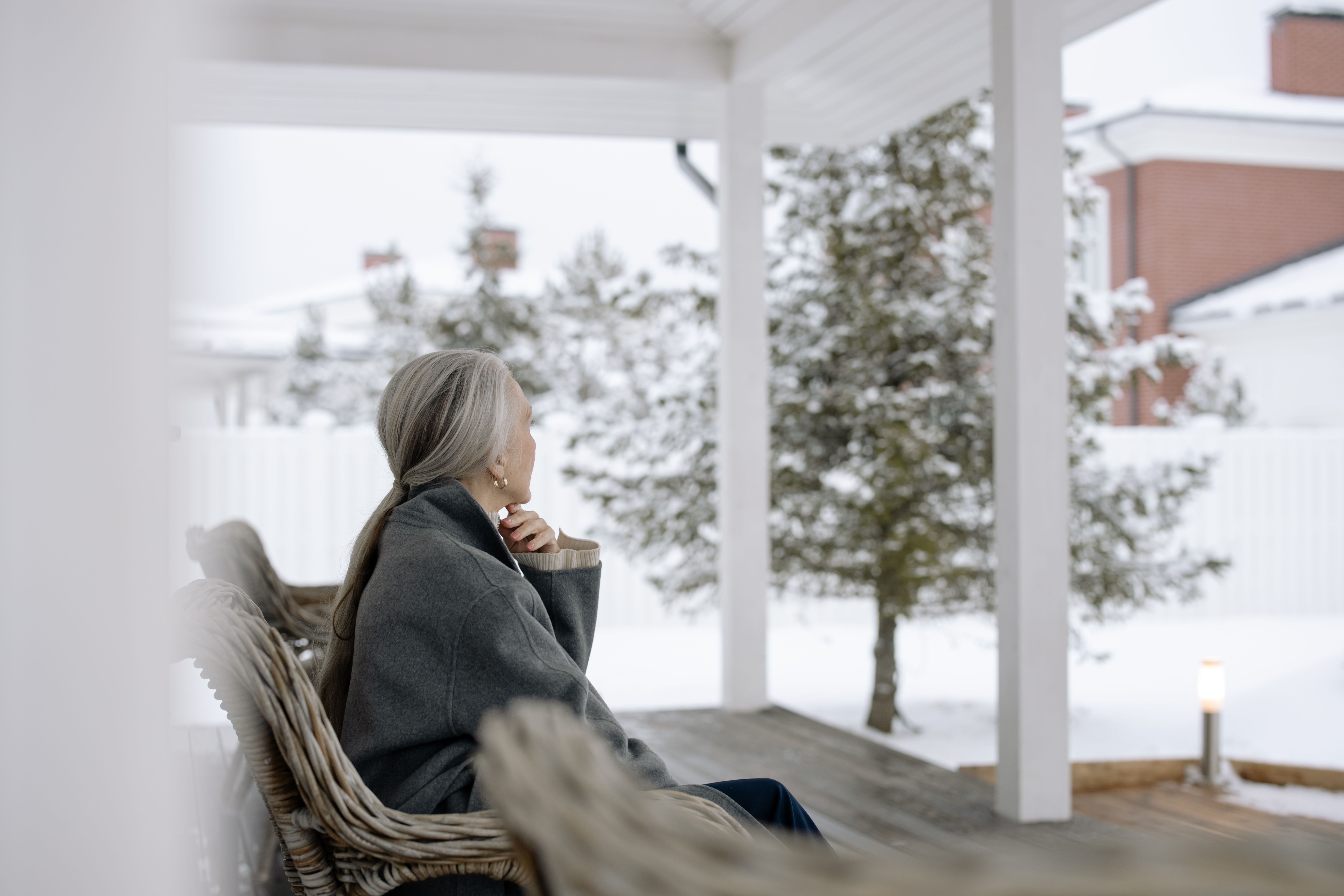 Senior woman sitting on porch in winter, enjoying serene snowy view.