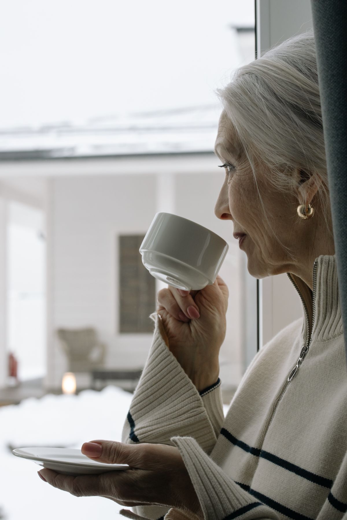 Woman with silver hair sipping coffee by a window in soft morning light