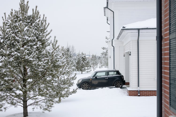 Car Parked In The Driveway In Front Of The House Among Snow 