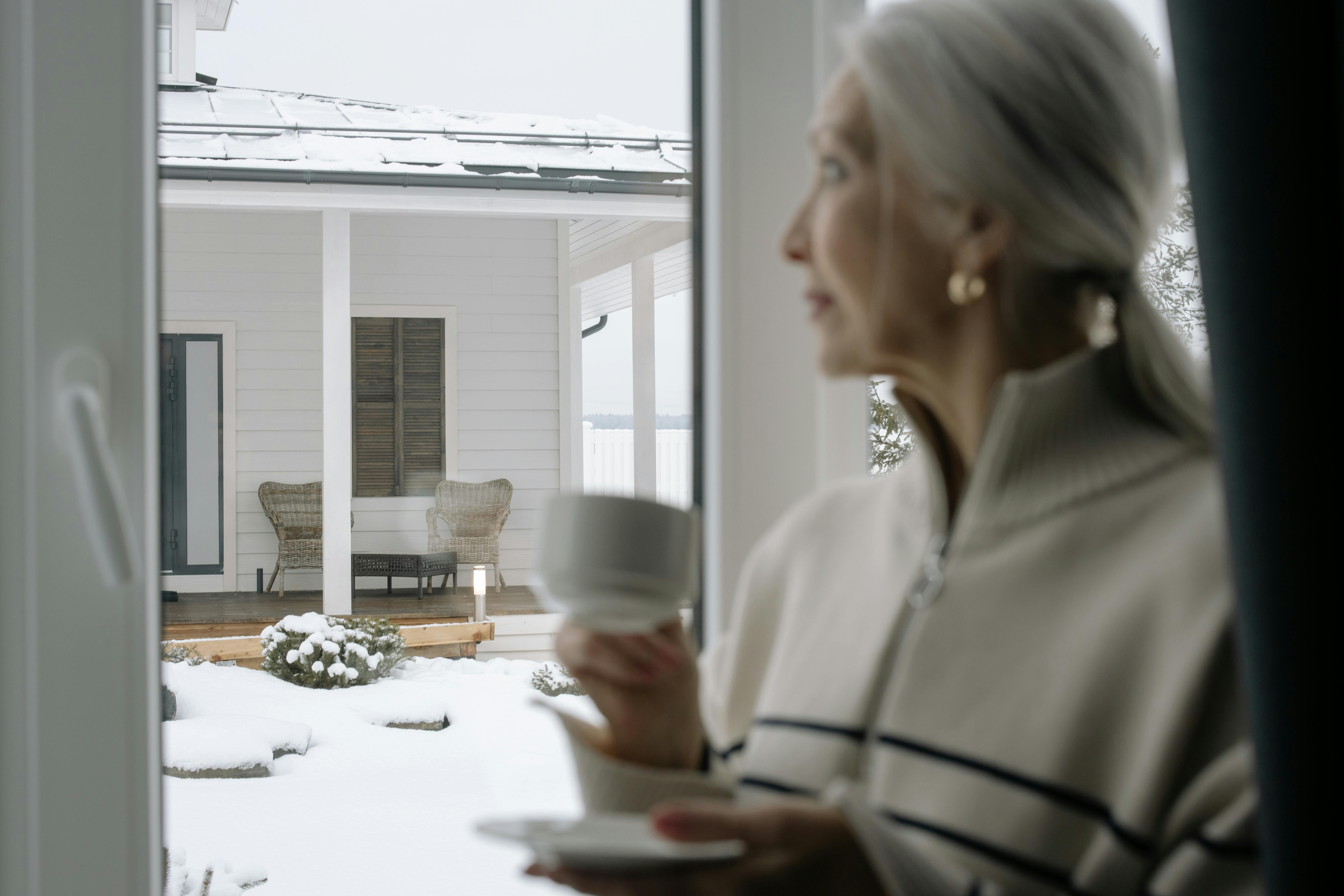 person holding a cup of coffee, looking out a window at a stormy sky, with a calm expression