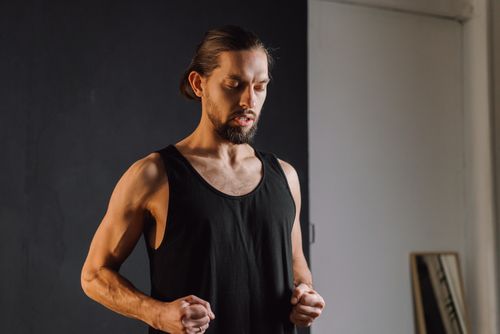 Free A bearded man in a sleeveless shirt practicing mindfulness indoors with closed eyes. Stock Photo