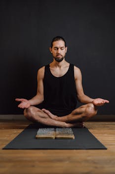 A man practicing meditation in a calm studio setting, seated on a yoga mat.