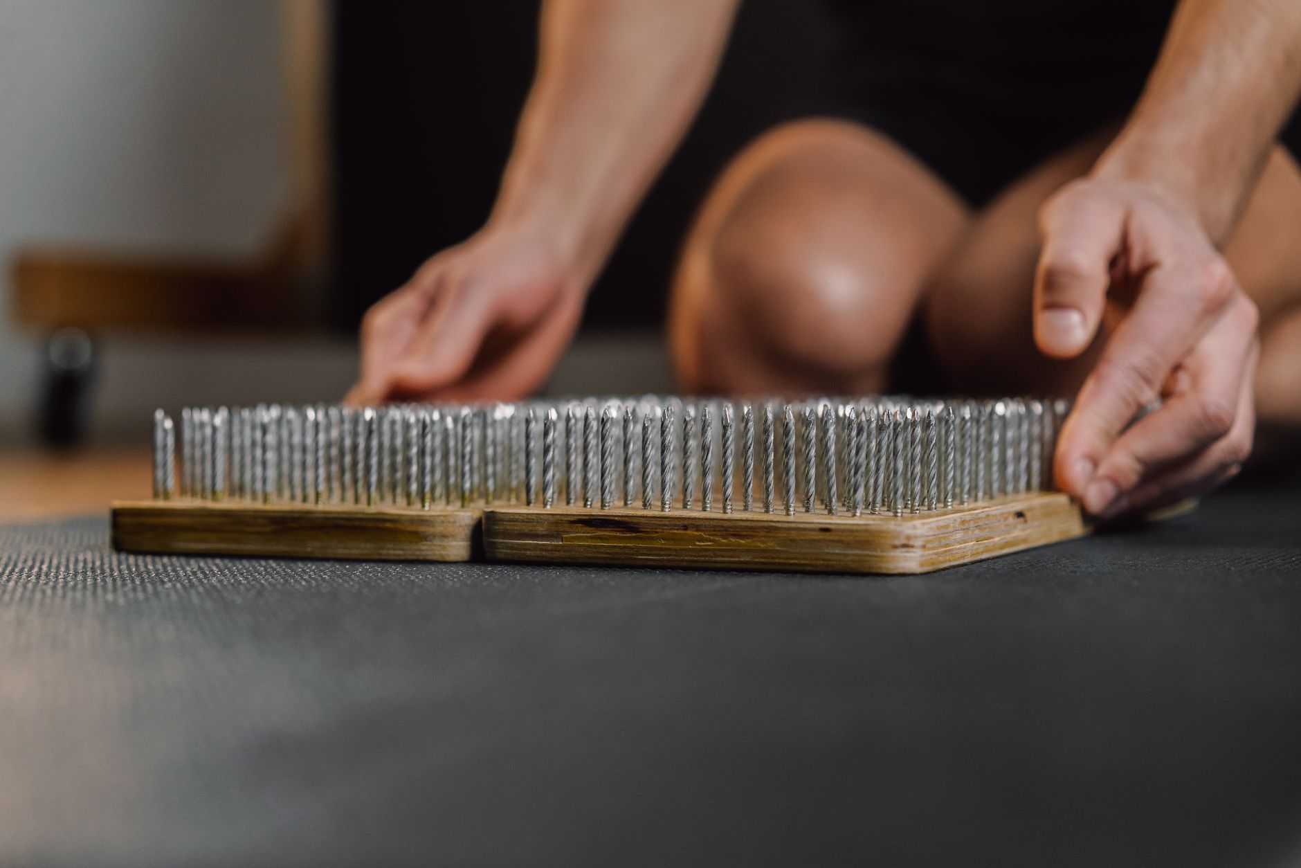 Close-up of hands handling a wooden bed of nails, used for meditation or exercise.