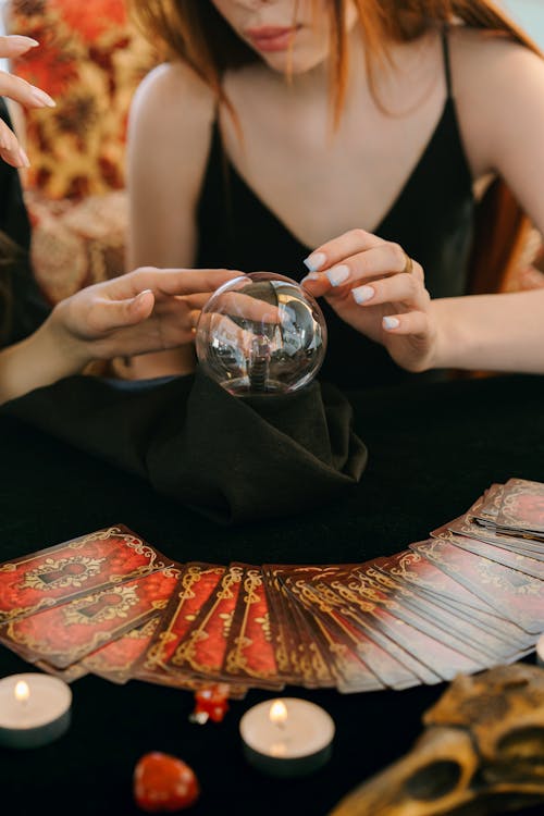 Free Crop unrecognizable female fortune tellers reading future with magical crystal ball and tarot cards during spiritual session Stock Photo