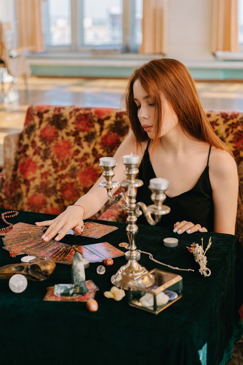 Concentrated female fortune teller with taro cards sitting at table with candlestick during mystical divination session