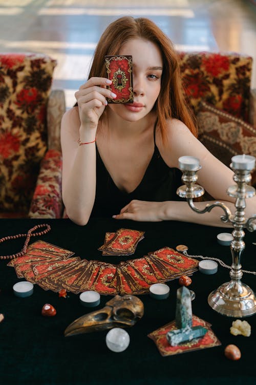 Free A Woman in Black Tank Top Holding a Tarot Card while Covering Her One Eye Stock Photo