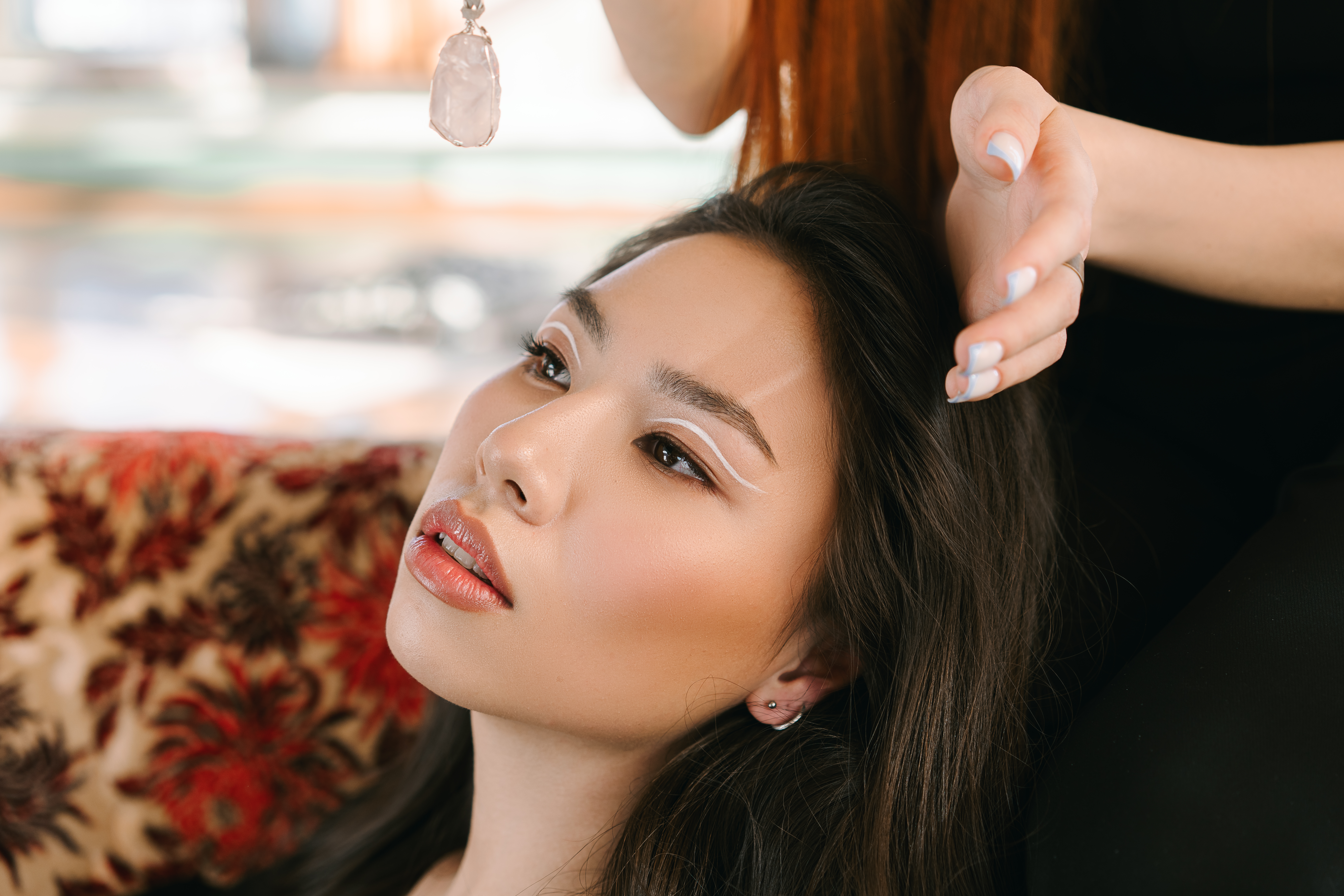 Asian woman with elegant makeup and crystal pendant, indoors setting.