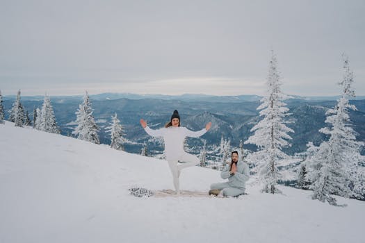 Two people meditating and practicing yoga outdoors in a snowy mountain landscape, embracing nature and tranquility.