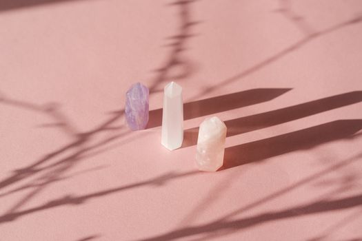 An artistic arrangement of crystals casting shadows on a soft pink background, creating a serene still life composition.