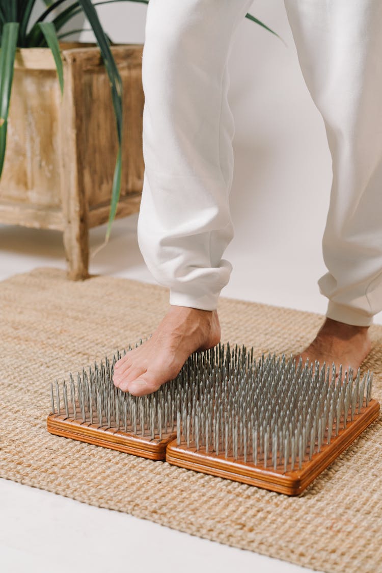 A Person In White Pants Stepping On Nail Boards Barefooted