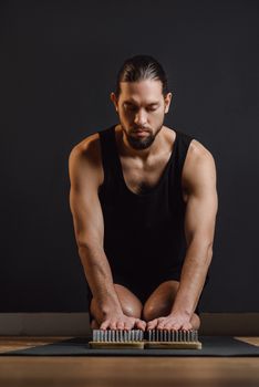 Focused man meditating in black tank top on a nail board. Indoor setting, calm atmosphere.