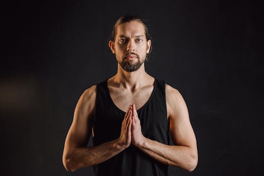 A bearded man in black tank top doing yoga, emphasizing mindfulness and fitness.
