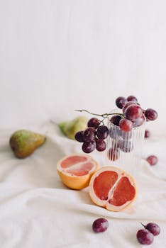 Artistic arrangement of grapes, grapefruit, and pear on a textured linen backdrop, emphasizing natural freshness.