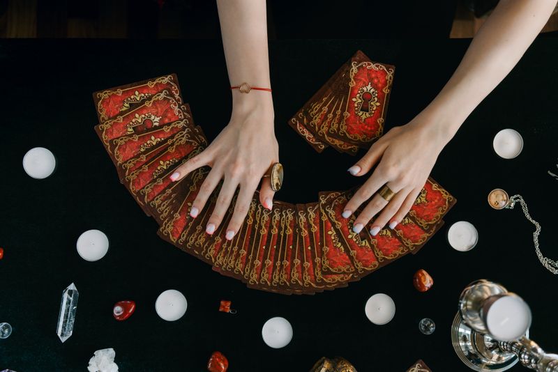 Hands fanning a tarot deck across a dark table