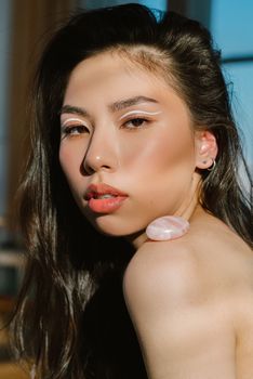 Side view of young ethnic woman with bare shoulder and long dark hair looking at camera