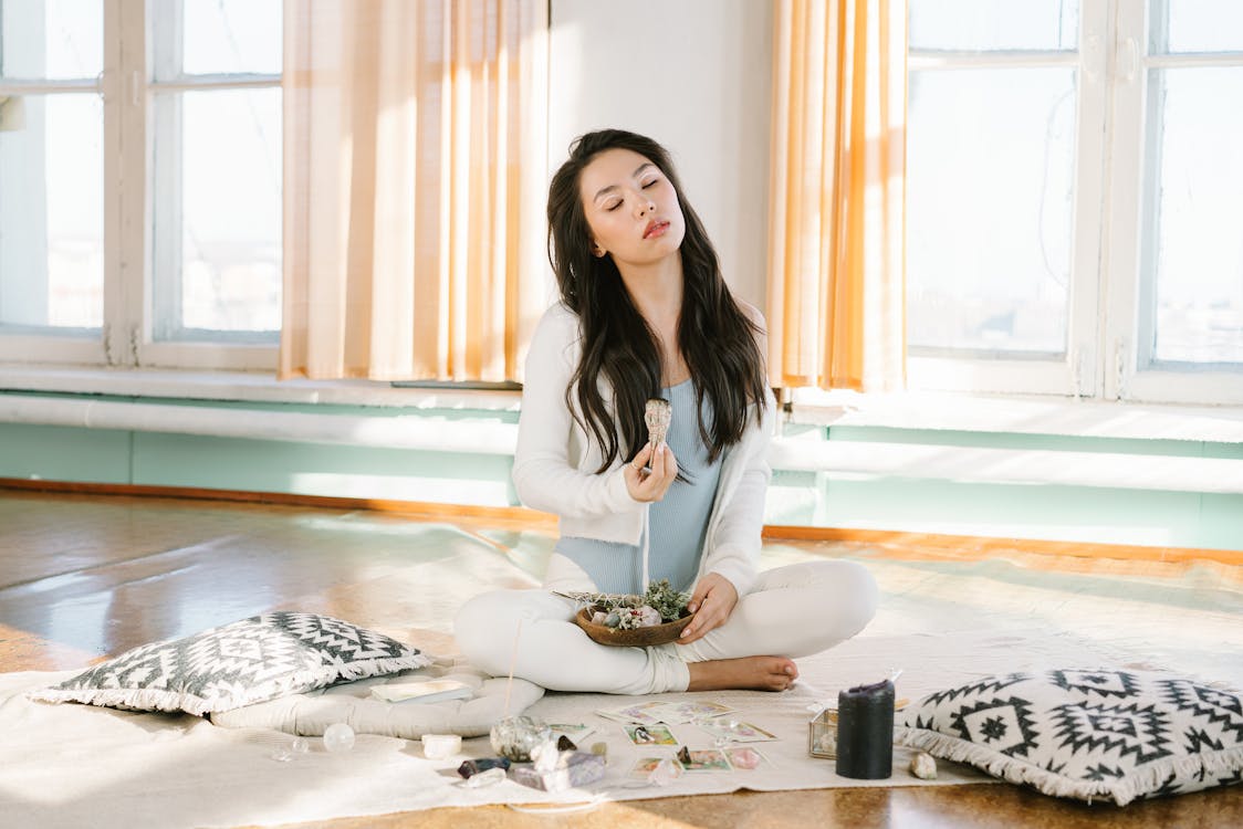 Full body of peaceful ethnic female smelling smoke from burning sage stick during spiritual session