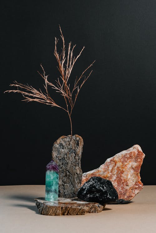 Composition of natural hard stones with dried branch of plant placed on table against black background