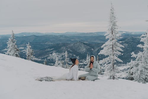 Peaceful couple meditating on snowy ground in highland