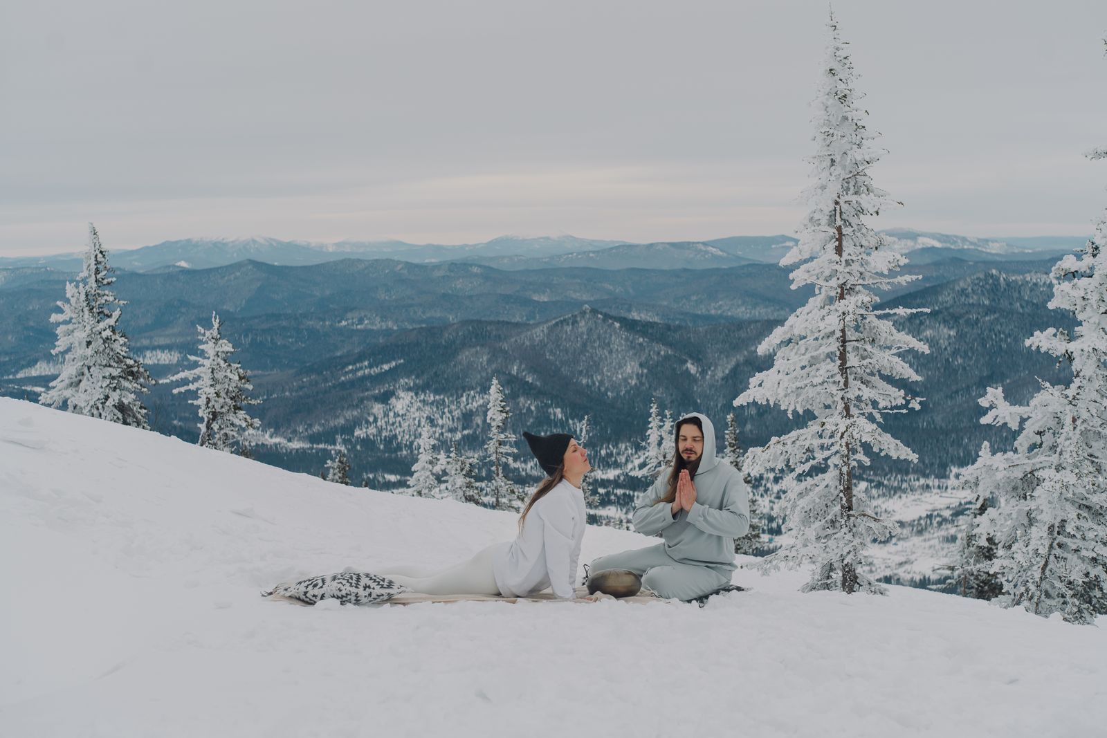 Woman practicing a yoga pose outdoors in a snowy mountain landscape during winter