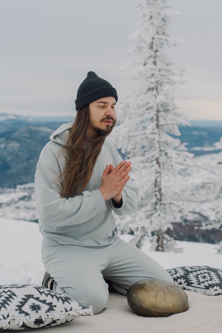 Man With Namaste Hands Sitting On Snow With Hapi Drum