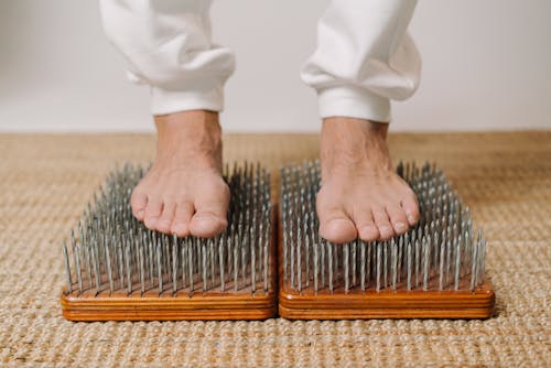 Crop unrecognizable male standing on wooden board with sharp metal nails for recovery and energy during spiritual session