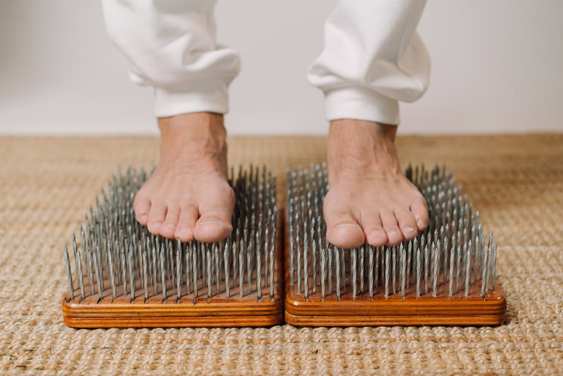 Free Crop unrecognizable male standing on wooden board with sharp metal nails for recovery and energy during spiritual session Stock Photo