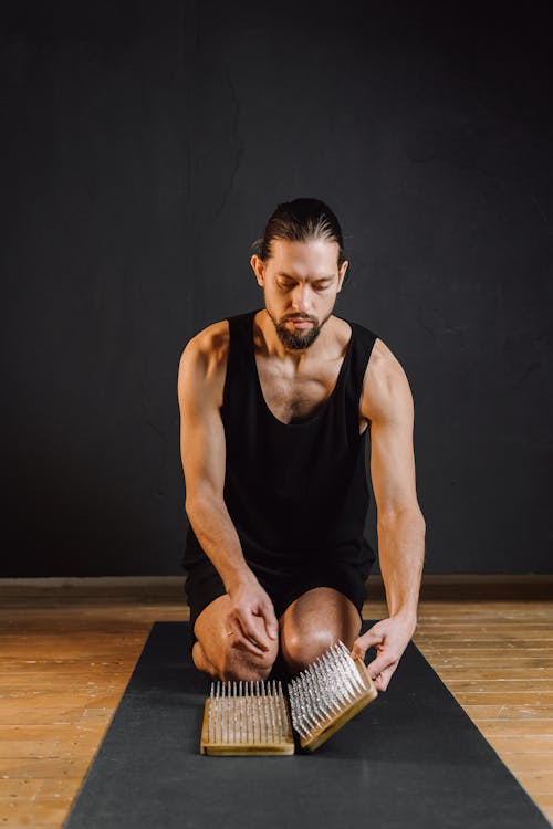 Serious bearded male in sportswear sitting on knees on sport mat with nail board for yoga practice