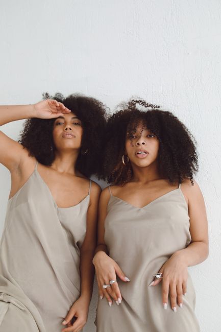 Chic photoshoot of two women with afro hair in stylish dresses posing against a white background.