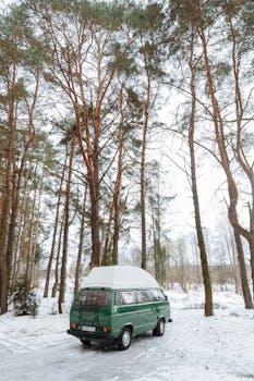 Green camper van parked in a snowy forest, ideal for winter road trips and outdoor exploration.