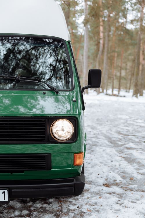 Free Close-up of a green campervan parked in a snowy forest, perfect for winter road trips. Stock Photo