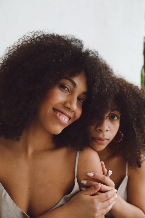 Free Beautiful portrait of two black women embracing, showcasing afro hair and fashion in a warm, intimate setting. Stock Photo