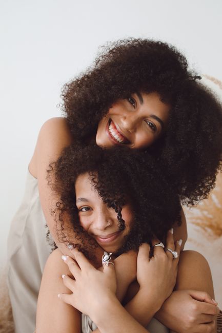 Two happy black women with afro hair embracing and smiling, radiating joy and love.