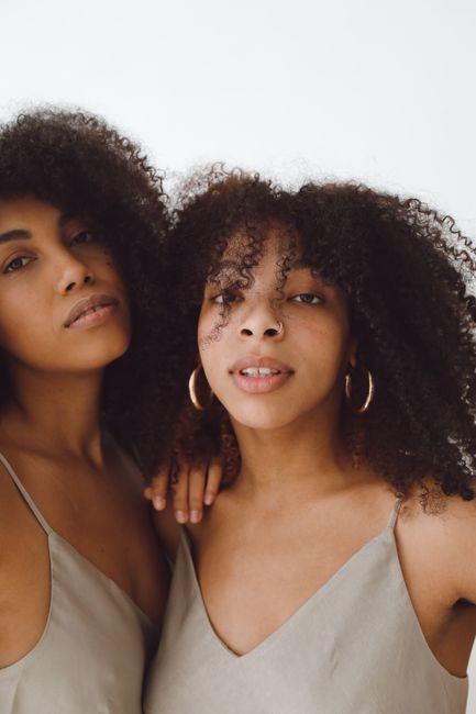 A close-up portrait of two women with afro hair in beige tops, showcasing natural beauty.