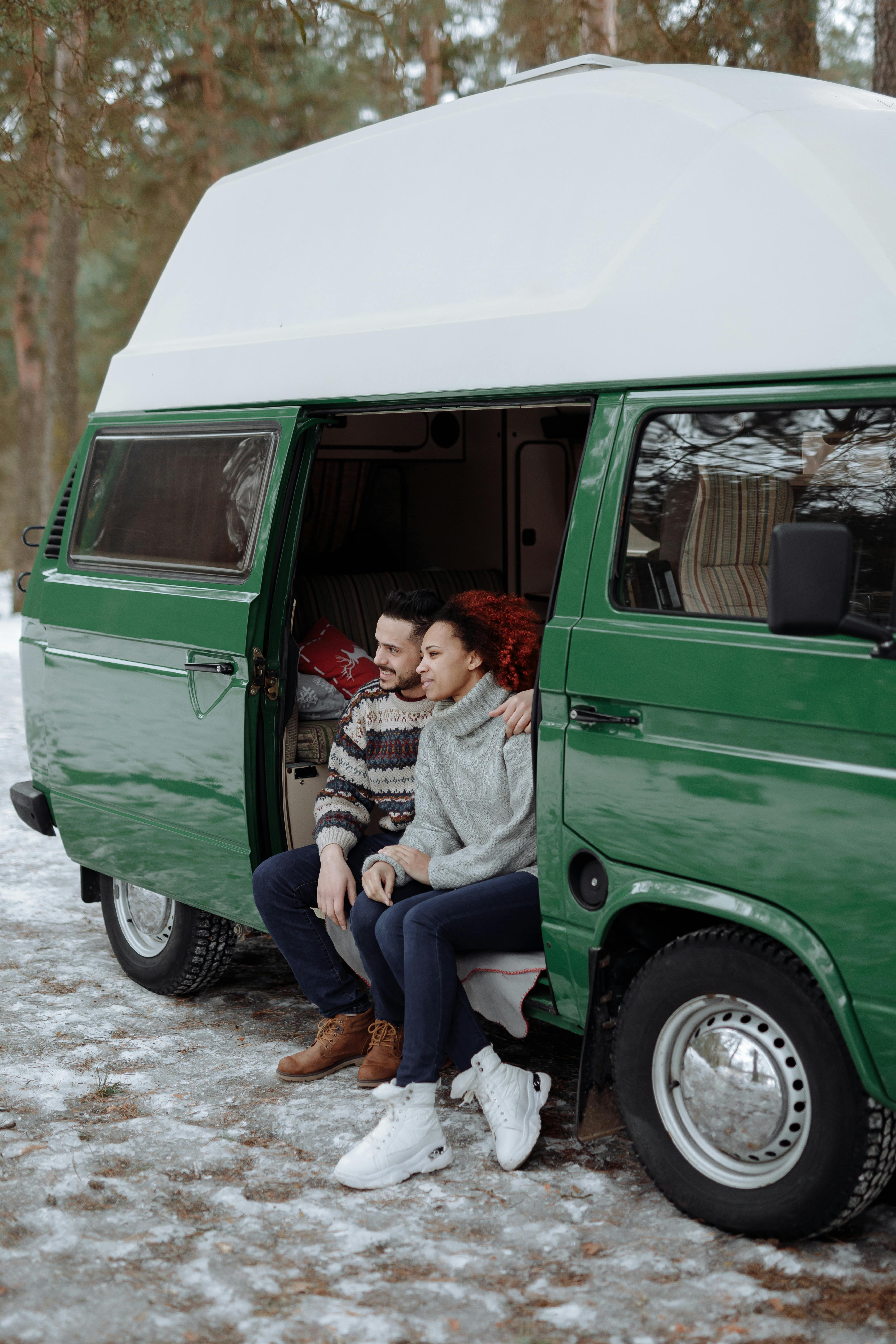 A couple enjoys a peaceful moment sitting in a camper van amidst a snowy forest setting.