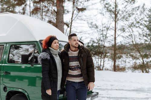 Free A couple enjoying a winter camping trip with their green campervan in a snowy forest. Stock Photo