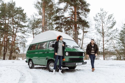 Free A couple enjoys a winter adventure with their green campervan in a snowy forest. Stock Photo