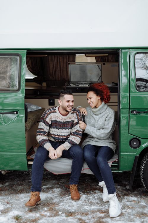 Free Couple sitting in a green camper van, enjoying a winter adventure together outdoors. Stock Photo