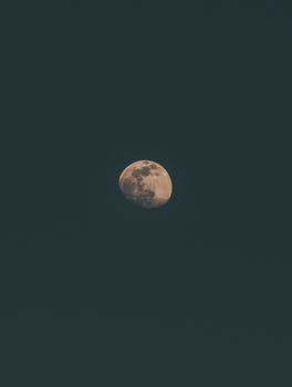 From below luminous moon in Waning Gibbous phase glowing on dark starless sky at night