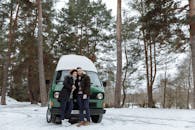 Man and Woman Sitting on Green Van on Snow Covered Ground