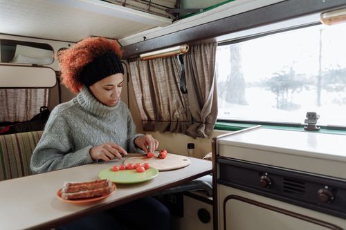 Free A woman chops cherry tomatoes in a camper van kitchen, showcasing a cozy van life scene. Stock Photo