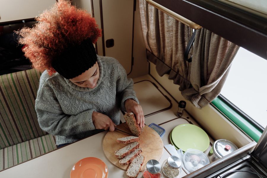 A woman with afro hair slices bread in a cozy camper van kitchen, enjoying van life.