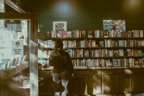 Free A person standing indoors, browsing books in a cozy bookstore with wooden shelves. Stock Photo