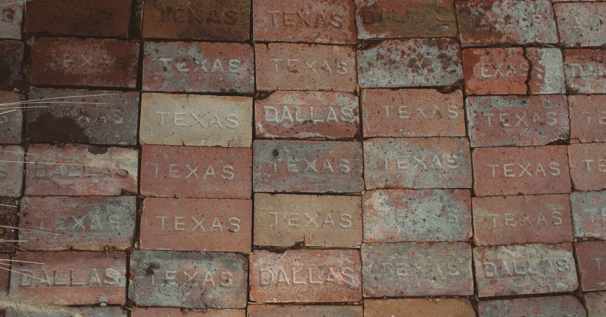 Close-up of stacked bricks engraved with 'Texas' and 'Dallas'. Rustic, textured surface.
