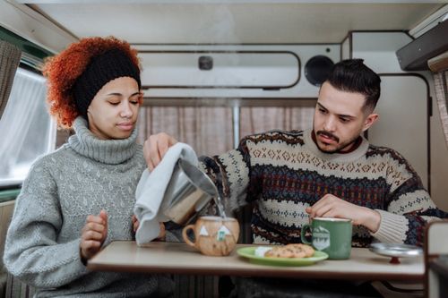 Free Friends enjoy a warm cup of tea and cookies inside a van on a relaxing road trip. Stock Photo